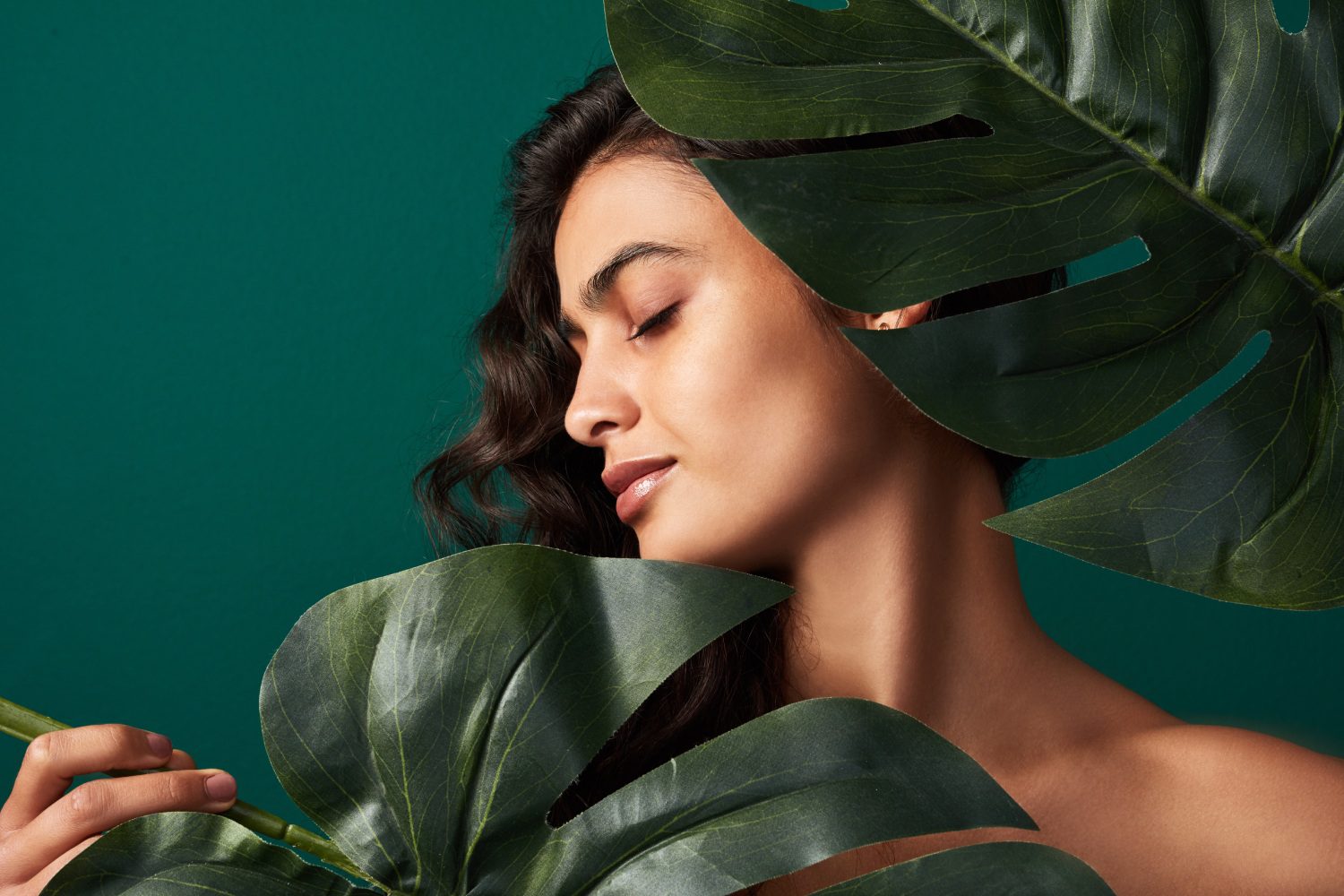 Woman with tropical leaves against green background.