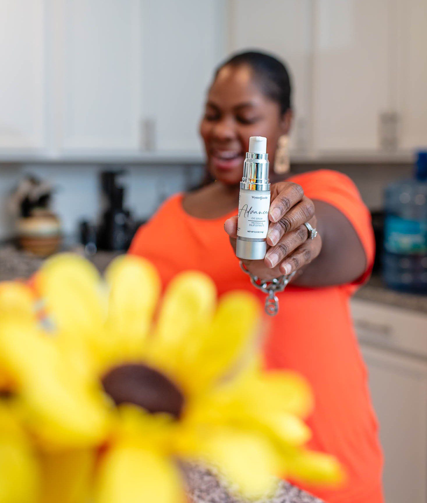 Woman holding skincare product, sunflower in foreground.